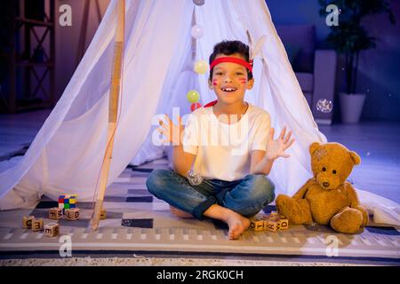 Photo d'adorable garçon doux jouant le jeu indien attrape des bulles dans la tente maison à l'intérieur salle de jeux du soir Banque D'Images