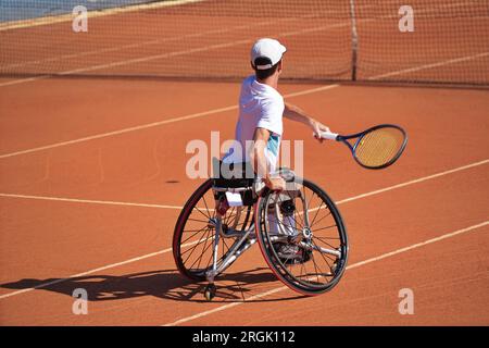 Homme pratique le tennis en fauteuil roulant sur un court de terre battue. Tennis en fauteuil roulant. Banque D'Images