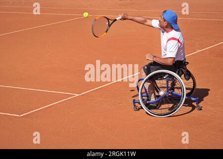 Homme pratique le tennis en fauteuil roulant sur un court de terre battue. Tennis en fauteuil roulant. Banque D'Images