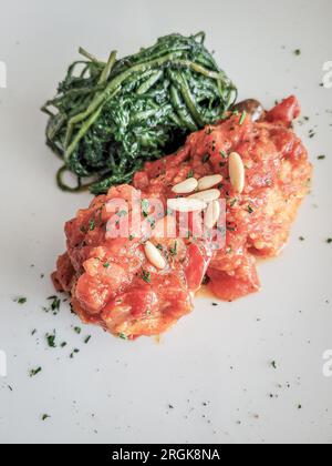 Poisson de morue romaine à la sauce tomate avec des pignons de pin et des légumes verts amers Banque D'Images