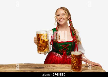 Jeune fille souriante portant un dirndl bavarois ou allemand traditionnel, tenant d'énormes lunettes sur fond blanc. Concept de l'Oktoberfest. Banque D'Images