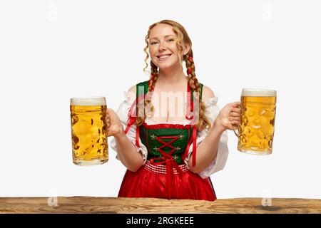 Jeune femme souriante habillée traditionnelle bavaroise ou allemande dirndl, tenant d'énormes lunettes de soleil sur fond blanc. Concept de l'Oktoberfest. Banque D'Images