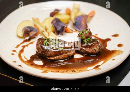 Grand angle de délicieux médaillons de bœuf grillé servis avec pommes de terre carottes et petits cors décorés avec sauce et oignon vert et servis dans un restaurant Banque D'Images