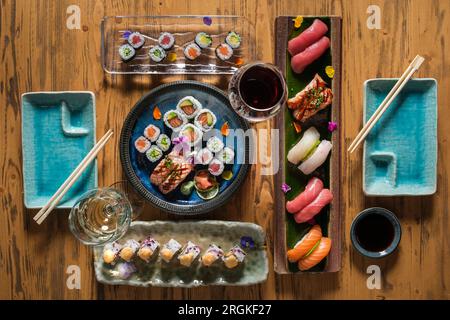 Vue de dessus de rouleaux de sushi japonais assortis avec baguettes et verres à vin avec vin rouge et blanc sur la table en bois Banque D'Images