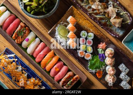 Vue de dessus de divers sushis frais et rouleaux avec différents poissons servis sur des plateaux en bois avec des crevettes dans un café léger Banque D'Images