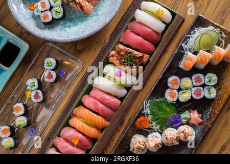 Vue de dessus de délicieux sushis traditionnels japonais et petits pains servis sur une assiette et des plateaux sur une table en bois dans un café léger Banque D'Images