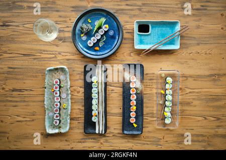 Vue de dessus de sushi assortis et rouleaux sur différentes assiettes en marbre placées sur une table en bois avec des baguettes et un verre à vin Banque D'Images
