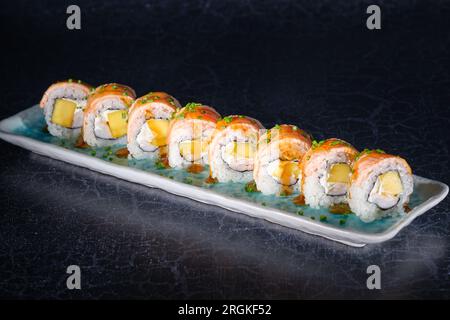 Délicieux rouleaux de sushi uramaki avec saumon frais servi et sauce sur plateau de marbre sur fond noir Banque D'Images