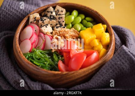 Grand angle de bol en bois avec des légumes frais, y compris tomates tranchées, fromage tofu radis et mangue servi avec salade d'algues et haricots edamame sur Banque D'Images