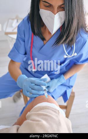 Grand angle de la récolte femelle médique dans le masque respiratoire inoculant le patient méconnaissable avec une seringue pendant une pandémie de coronavirus Banque D'Images