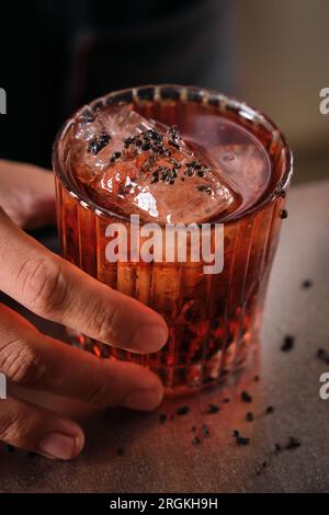 Du dessus de la récolte méconnaissable barman servant un cocktail rafraîchissant Negroni avec des glaçons et du chocolat râpé dans le verre de roches sur le comptoir gris dans le bar Banque D'Images