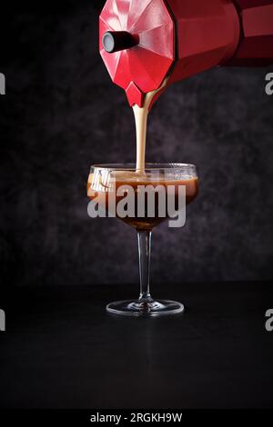 Barman inreconnaissable remplissant le verre coupé transparent de campagne avec un cocktail de café frais fait à partir d'un pot de moka dans le bar sombre Banque D'Images