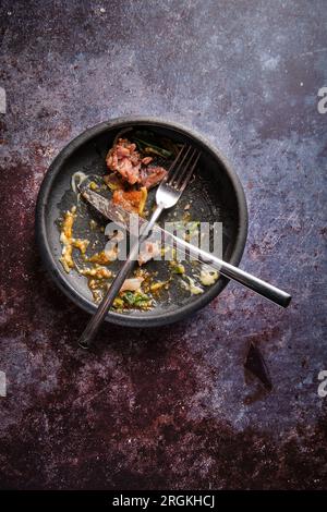 Vue de dessus des couverts métalliques croisés placés sur une assiette sombre sale sur une table grise vieillie Banque D'Images