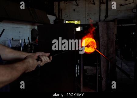 Verrerie masculine méconnaissable mettant la pipe de soufflage en métal avec le verre chauffé sous forme de vase narguilé sur la pointe dans le four de recuit tout en travaillant à l'usine Banque D'Images