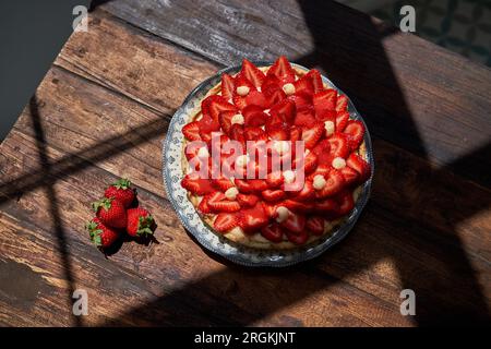 D'en haut gros plan du motif de décoration de délicieuses fraises sur la croûte de tarte et plaçant dans la plaque de céramique sur la table en bois à la lumière du jour à travers Windo Banque D'Images