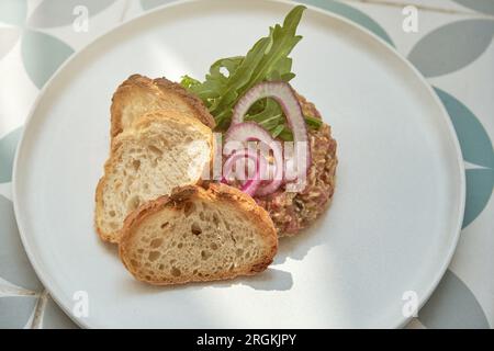 Angle élevé de steak tartare appétissant décoré avec des tranches d'oignons rucola et croûtons et placé sur sol carrelé Banque D'Images