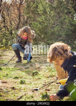 Des adolescents bénévoles concentrés ramassent les déchets et les déchets plastiques du sol dans la forêt en journée ensoleillée Banque D'Images