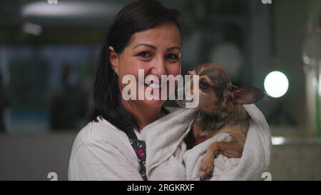 Portrait d'une femme tenant le chien enveloppé dans une serviette debout à l'intérieur de PET Shop. Joyeuse femme propriétaire de petite entreprise de magasin local. Service de profession c Banque D'Images