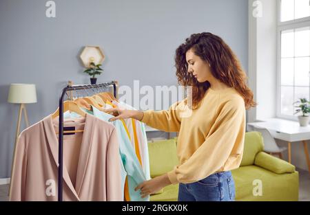 Jolie jeune femme choisissant des vêtements à la garde-robe à la maison Banque D'Images