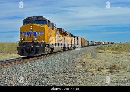 Un train de marchandises de l'Union Pacific manifeste en direction de l'ouest est vu approchant du passage routier Parkside Drive à Desert Beach Southern California. Banque D'Images