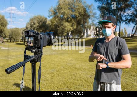Un blogueur masculin portant un masque de protection regarde la caméra et parle dans une rue de la ville. Banque D'Images