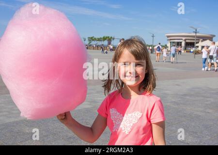 Fille heureuse tenant des bonbons de coton dans un parc d'attractions Banque D'Images