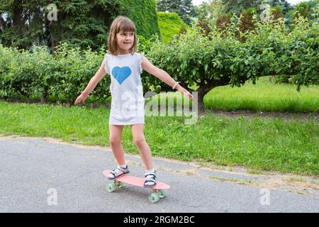 Petite fille dans le parc apprend à monter un skateboard Banque D'Images