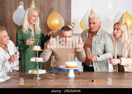 Homme mature avec ses amis faisant souhait à la fête d'anniversaire dans la cuisine Banque D'Images