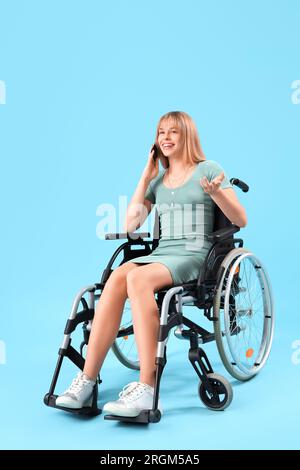 Jeune femme en fauteuil roulant parlant par téléphone portable sur fond bleu Banque D'Images