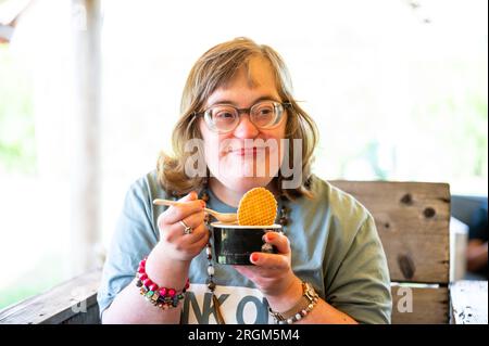 Portrait d'une femme de 40 ans avec le syndrome de Down mangeant une crème glacée, Meerhout, Belgique Banque D'Images