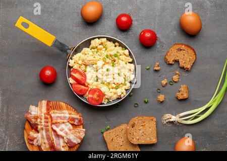 Poêle à frire de savoureux œufs brouillés avec des tomates et du bacon sur fond gris Banque D'Images