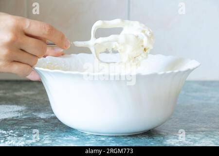 Nous battons les œufs avec du sucre sur un mélangeur dans une assiette sur la table dans la cuisine, en préparant la pâte pour la tarte Banque D'Images