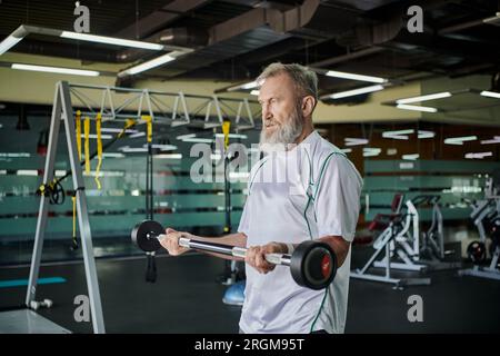 homme âgé athlétique avec barbe s'exerçant avec barbell dans la salle de gym, senior actif, athlète, force Banque D'Images