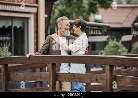 couple senior romantique debout ensemble sur un pont en bois et se serrant les uns les autres, amour âgé, lien Banque D'Images