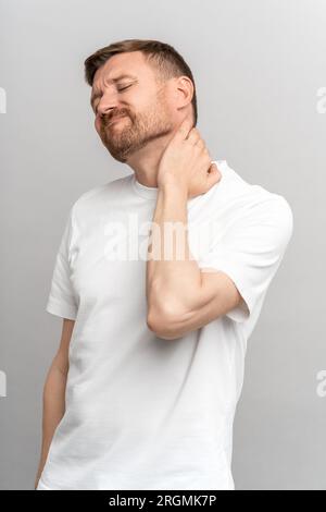 L'homme malheureux froncé ressent une douleur sévère dans le cou essayant d'étirer les muscles dans la colonne vertébrale sur le mur gris du studio Banque D'Images