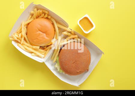Ouvrir la boîte en carton avec des hamburgers et des frites sur un fond jaune, vue de dessus. Restaurant de restauration rapide Banque D'Images