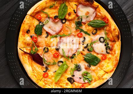 Pizza avec jerky, olives, fromage et herbes sur un plat rond noir de cuisson, vue de dessus. Cuisine italienne traditionnelle. Banque D'Images