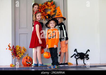 Les enfants trichent ou gâtent le soir d'Halloween. Les enfants habillés à la porte de la maison décorée. Garçon et fille en costume de sorcière et de vampire et chapeau Banque D'Images