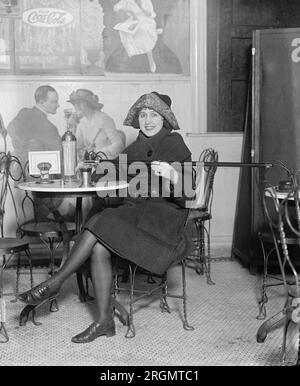 Femme assise à une table de fontaine de soda verse de l'alcool dans une tasse d'une canne, pendant la prohibition ; avec une grande publicité Coca-Cola sur le mur ca. 1922 Banque D'Images