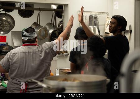 Reportage : SNAP emploi et formation au café Reconcile à la Nouvelle-Orléans LA (février 2023) - à gauche, un formateur défenseur de la cuisine, de la pâtisserie et du service au café Reconcile, donne un High Five à un stagiaire de 20 ans, avant l'ouverture du restaurant à la Nouvelle-Orléans, la, le 16 février 2023. Banque D'Images