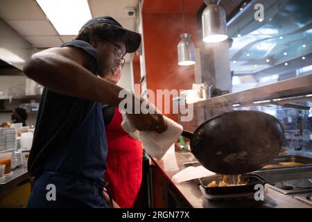 Reportage : SNAP emploi et formation au café Reconcile à la Nouvelle-Orléans LA (février 2023) - Un stagiaire de 20 ans au café Reconcile verse une portion chaude de nourriture pour un client à la Nouvelle-Orléans, la., le 16 février 2023. Banque D'Images