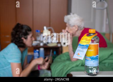 Berlin, Allemagne. 31 juillet 2023. Une bouteille d'eau avec l'inscription « Sunny Heat! Buvez plus ! » Et le logo de Diakonie Schöneberg se tient près du lit de soins pendant que l’infirmière Ramona Rössner parle à sa patiente, Brigitte Richter, âgée de 97 ans, qui a besoin de soins, lors d’une visite à domicile. (À dpa-KORR 'Tu bois, je bois' - Comment la chaleur met en danger les personnes âgées) crédit : Monika Skolimowska/dpa/Alamy Live News Banque D'Images