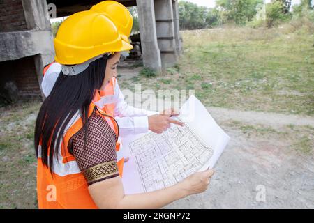 Deux ingénieurs civils indiens hommes et femmes ou un architecte portant casque et gilet tenant le plan de paperasse sur le chantier de construction discutant du vrai estat Banque D'Images
