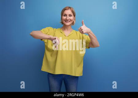 femme mûre blonde énergique dans le haut de réservoir jaune montre comme avec les mains Banque D'Images