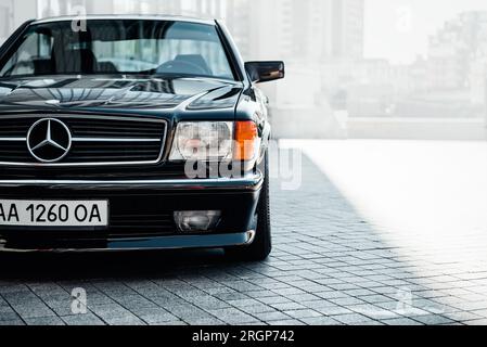 Classique Mercedes-Benz W126 noir. Vue de coin avant du coupé de luxe Mercedes-Benz SEC des années 1980 garé près d'un immeuble de bureaux générique. Banque D'Images