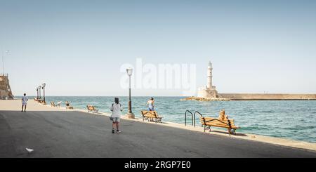 Promenade maritime dans le port de la Canée avec vue sur le phare et le brise-lames. Peu de piétons marchent le long de la promenade du vieux port par une journée ensoleillée. Banque D'Images