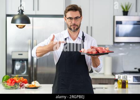 Concept de steak de bœuf. Homme d'âge moyen cuisinant de la viande, steak de bœuf dans la cuisine. Homme sur la cuisine avec de la viande et du bœuf cru. Banque D'Images
