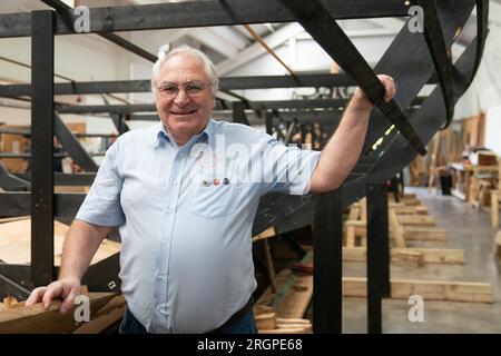 Maître constructeur de navires Tim Kirk avec la réplique du Sutton Hoo, au Longshed à Woodbridge, Suffolk. Trois apprentis menuisiers entreprennent un stage de deux semaines avec la Sutton Hoo Ship's Company, qui dirige les travaux sur la réplique grandeur nature de 88 pieds de long. Date de la photo : Vendredi 11 août 2023. Banque D'Images