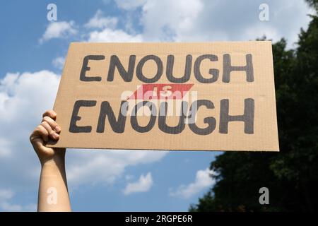 Femme tenant pancarte signe assez est assez. Banderole en carton lors d'une manifestation de protestation. Appelez au changement, exigez une action en matière de justice sociale. Banque D'Images