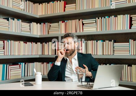 Homme prenant une pilule de médicament de migraine de mal de tête. Maux de tête et fatigue oculaire sur ordinateur portable. Homme d'affaires avec stress et fatigue oculaire. Homme d'affaires Banque D'Images